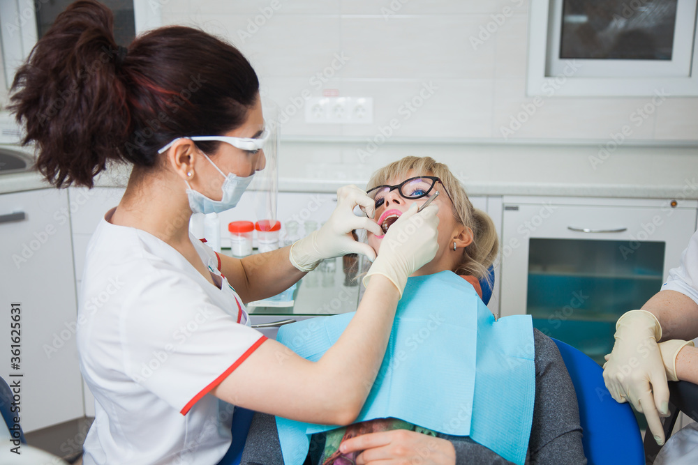 Female dentist work with light-curing seal cofferdam, patient with caries on chair. Stomatologist and patient at clinical office. Toothcare concept Female dentist work with light-curing seal cofferdam, patient with caries on chair. Stomatologist and patient at clinical office. Toothcare concept