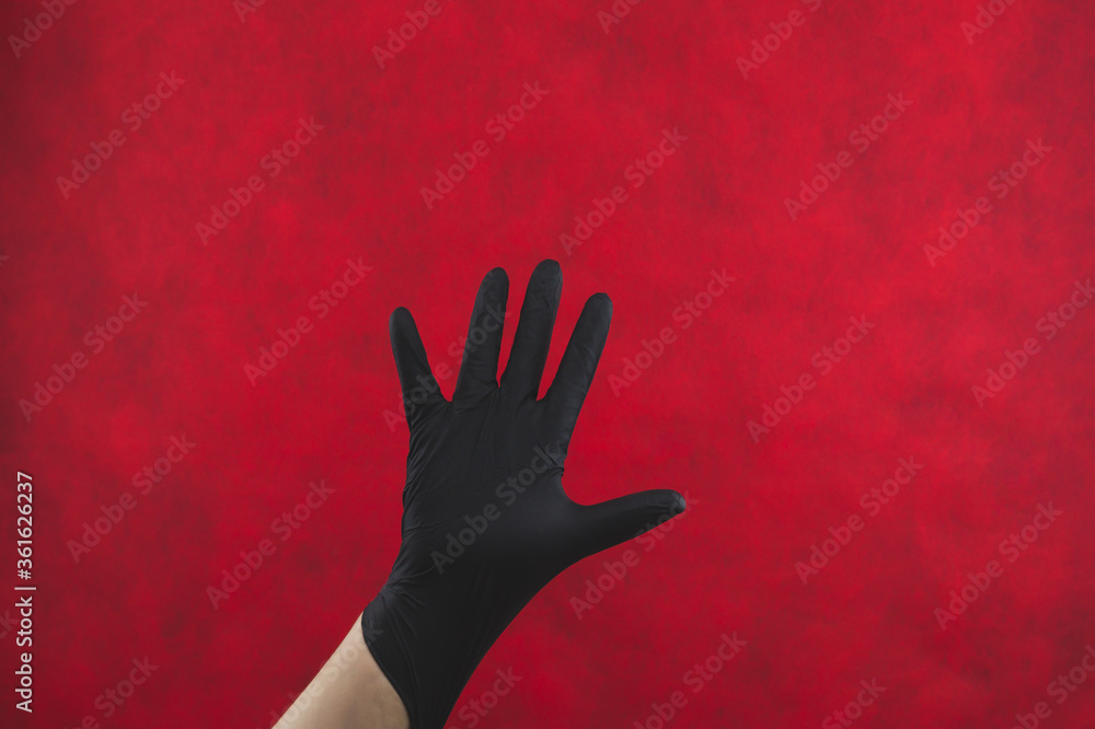 Palm of hand in medical glove on a red background. gesturing hand in black protective glove Palm of hand in medical glove on a red background. gesturing hand in black protective glove