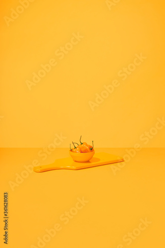 Hot Habanero Peppers in Bowl on Cutting Board on Table Top Yellow Surface and Background.  Monochromatic  Set photo