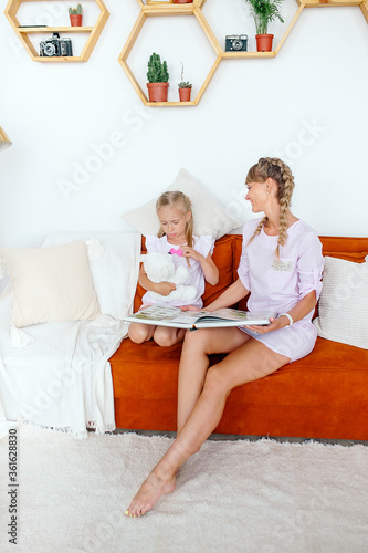 Attractive mother. Little adorable daughter sitting on the sofa in the living room at home reading the end of a book fairy tale. Weekend events and development concept