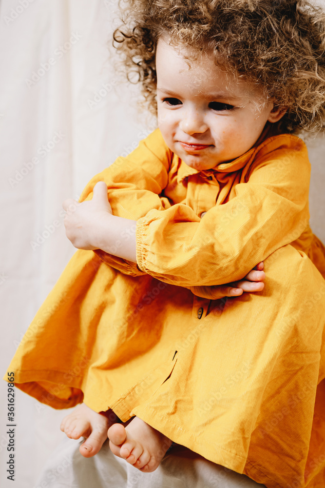 Portrait of a little curly girl with freckles dressed in a yellow dress Home family fun parents with baby.