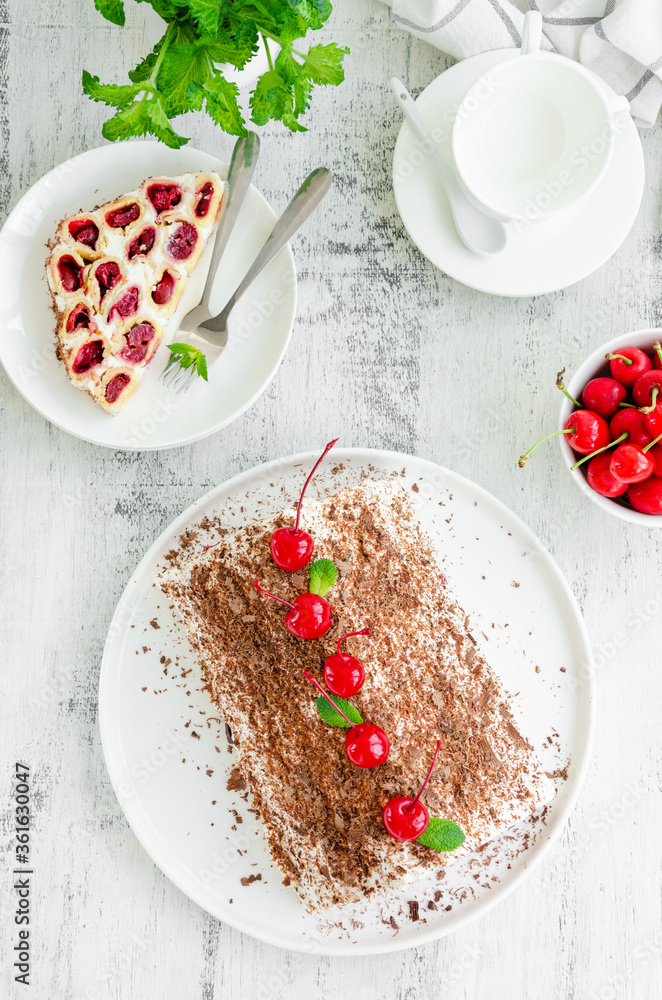 Homemade cake with cherries, sour cream and chocolate on a white plate on a wooden background. Vertical, copy space. Homemade cake with cherries, sour cream and chocolate on a white plate on a wooden background. Vertical, copy space.
