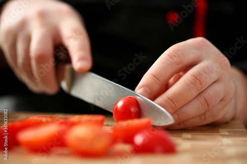 Cook holds knife in hand and cuts on cutting board red tomatoes for salad or fresh vegetable soup with vitamins. Raw food and vegetarian recipe book in modern society popular concept.
