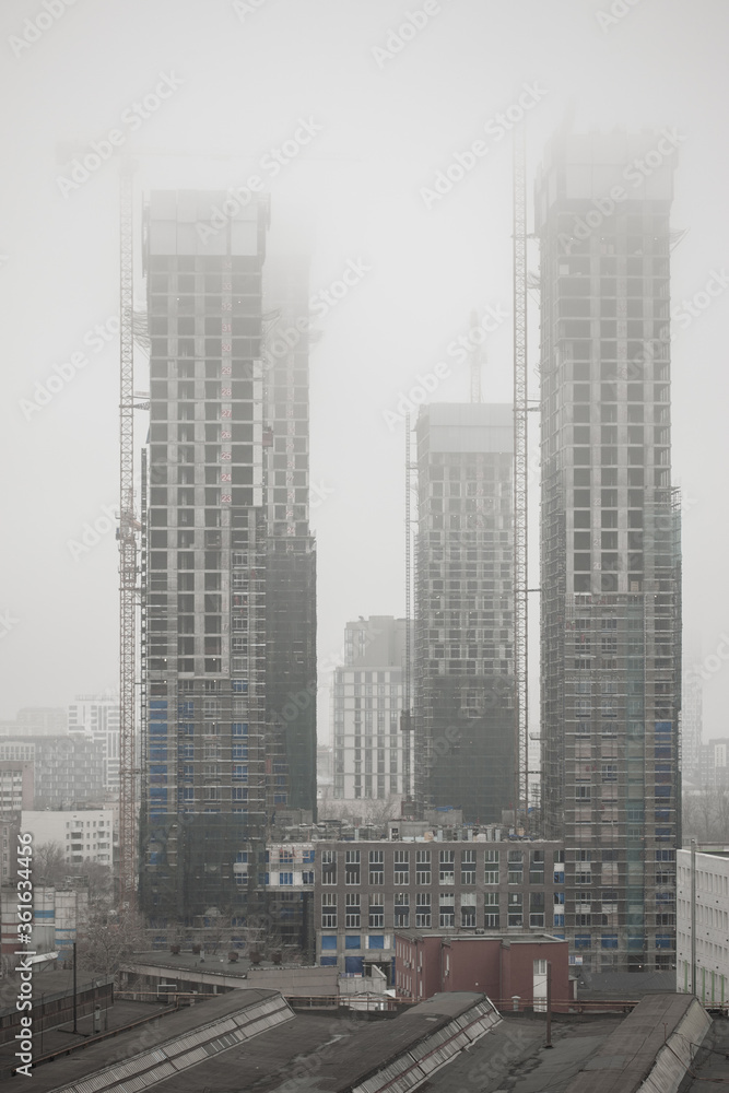 Urban landscape with low cloud and smog. High rise building under construction. A construction crane lifts rebar to the upper floors of a skyscraper. Selective focus
