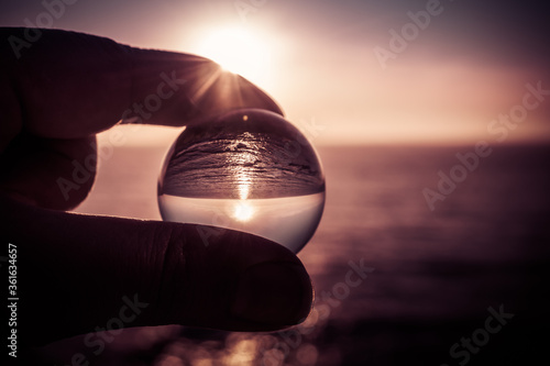 Fingers holding ball lens with sea landscape of Porto Barril beach in monochrome tones with shining sun, Encarnação - Mafra PORTUGAL
