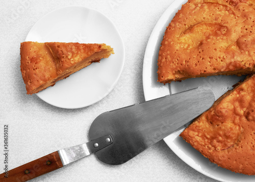 Applepie on the plate with cake server and slice of cake on saucer on light background, top view