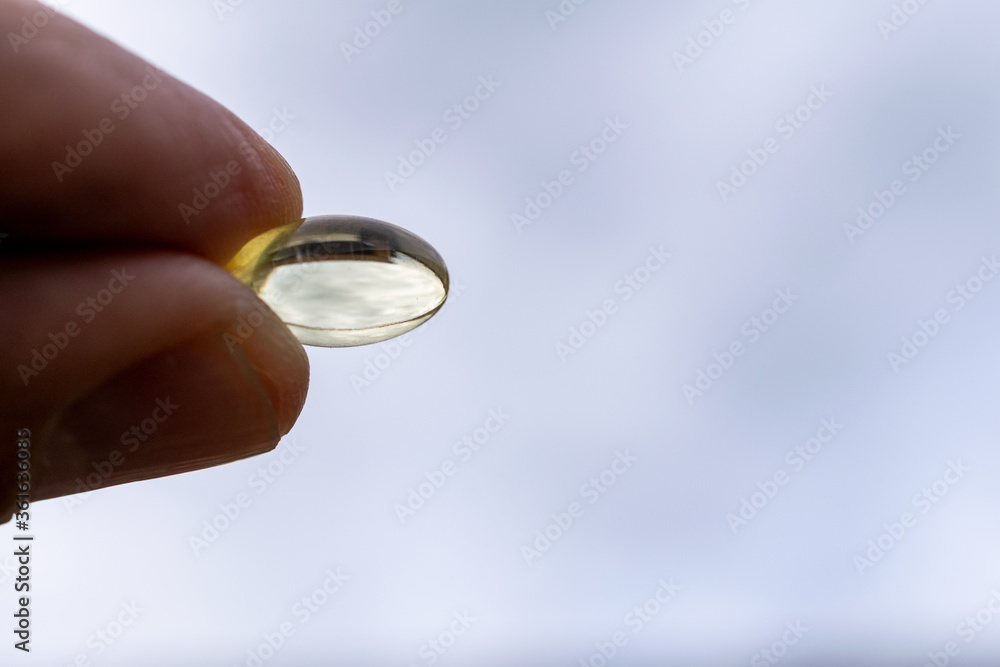 vitamin d, fingers holding capsule, with blue sky background. vitamin d, fingers holding capsule, with blue sky background.