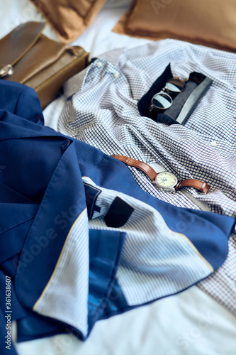 Close-up of men's businesswear and a wristwatch on the bed.