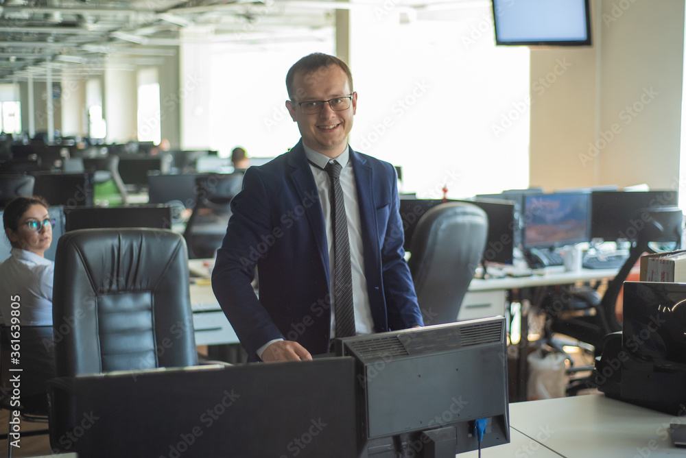 Happy male employee at the workplace in the office Open Space. Friendly business man in a suit at his desk. Work in Modern office. Happy male employee at the workplace in the office Open Space. Friendly business man in a suit at his desk. Work in Modern office.