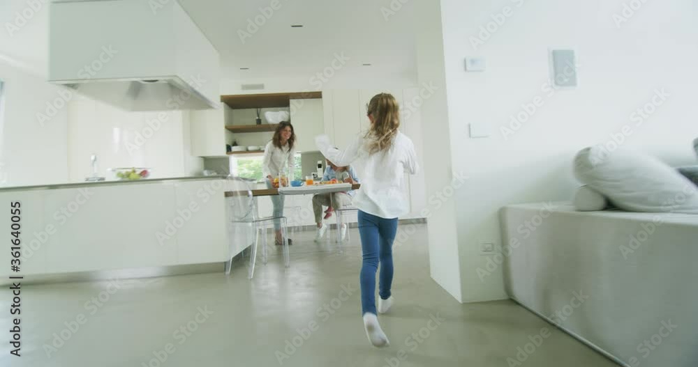 Authentic shot of a happy smiling family is enjoying their time together while having a breakfast in a kitchen at home in the morning. A bigger daughter is arriving and giving a hug to her mother. Authentic shot of a happy smiling family is enjoying their time together while having a breakfast in a kitchen at home in the morning. A bigger daughter is arriving and giving a hug to her mother.