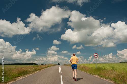 athlete runs up the road on a sunny day against the background of nature