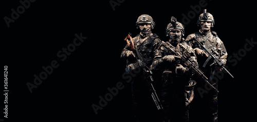 Obraz na plátne Three soldiers in uniform with a weapon in their hands are looking menacingly