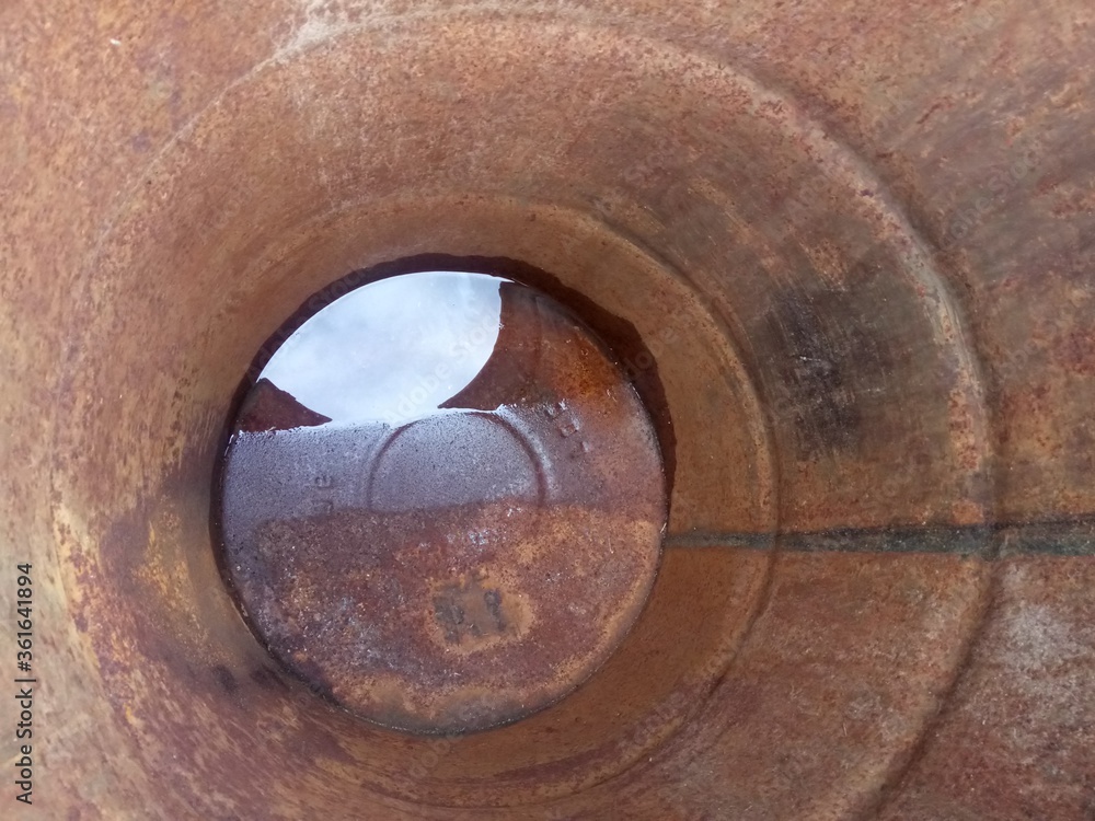 reflection of a cloudy sky in water at the bottom of a rusty barrel