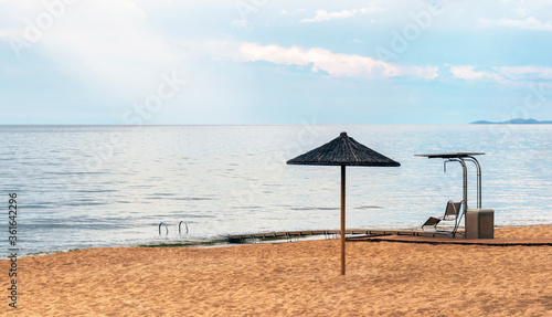 Lonely deck chair, beach umbrella and path to sea on deserted beach near the town of Kavala, Greece. Enjoying time alone in nature concept. Calming seascape. Copy space for text