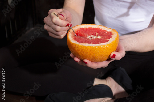 Half a large red grapefruit in the hands of a ballerina with a spoon against the background of ballet shoes