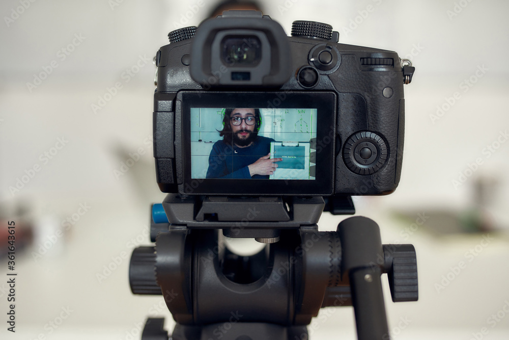 Video tutorial. Young man wearing glasses looking at camera while giving online class, recording online lesson on professional digital equipment