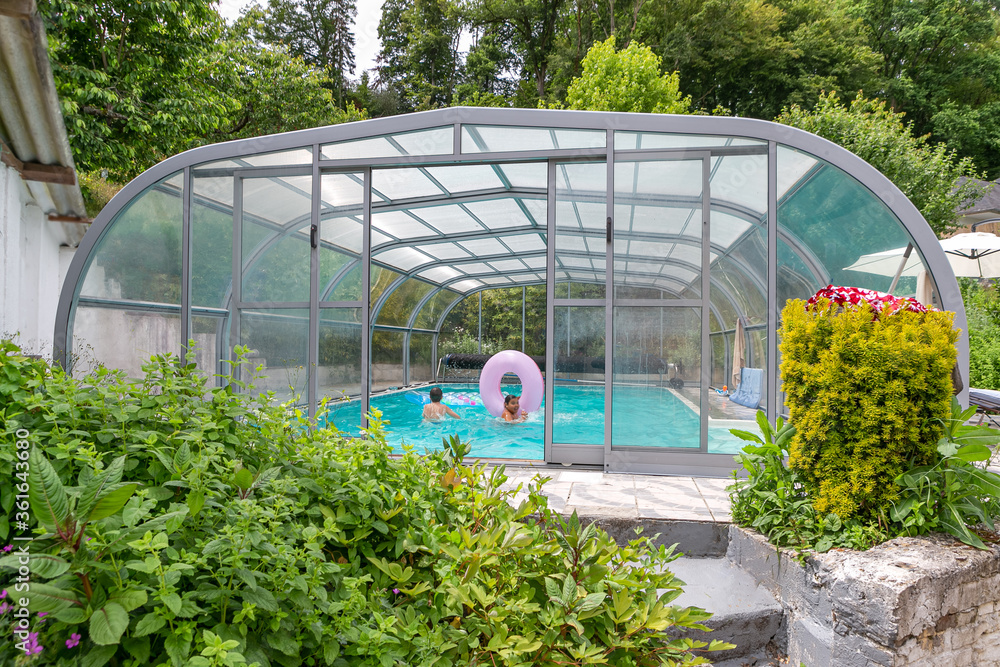Fototapeta premium Swimming pool with a roof with kids playi,g inside oin a garden