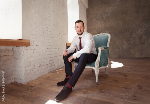  a man in a shirt and tie sits on an armchair