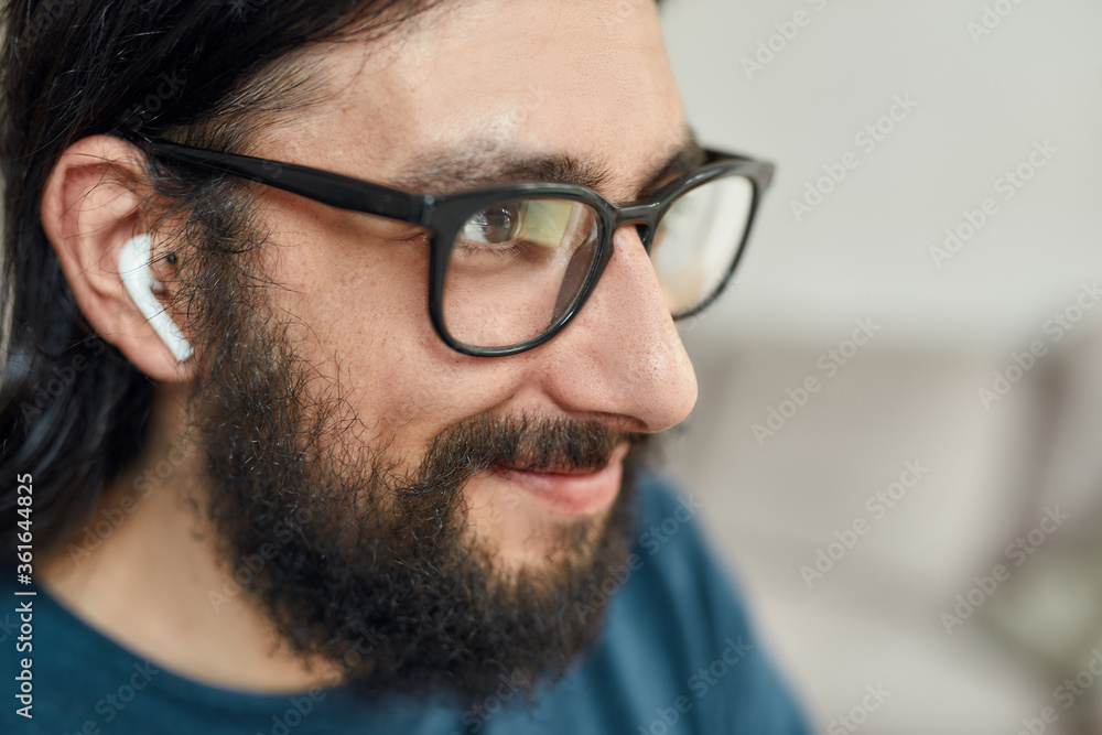 Close up of happy caucasian bearded man wearing eyeglasses and wireless headphones working from home. Stay home, self isolation Close up of happy caucasian bearded man wearing eyeglasses and wireless headphones working from home. Stay home, self isolation