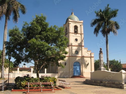 Main square in Viñales with small cream-colored church surrounded by palm trees, Cuba © Slawina