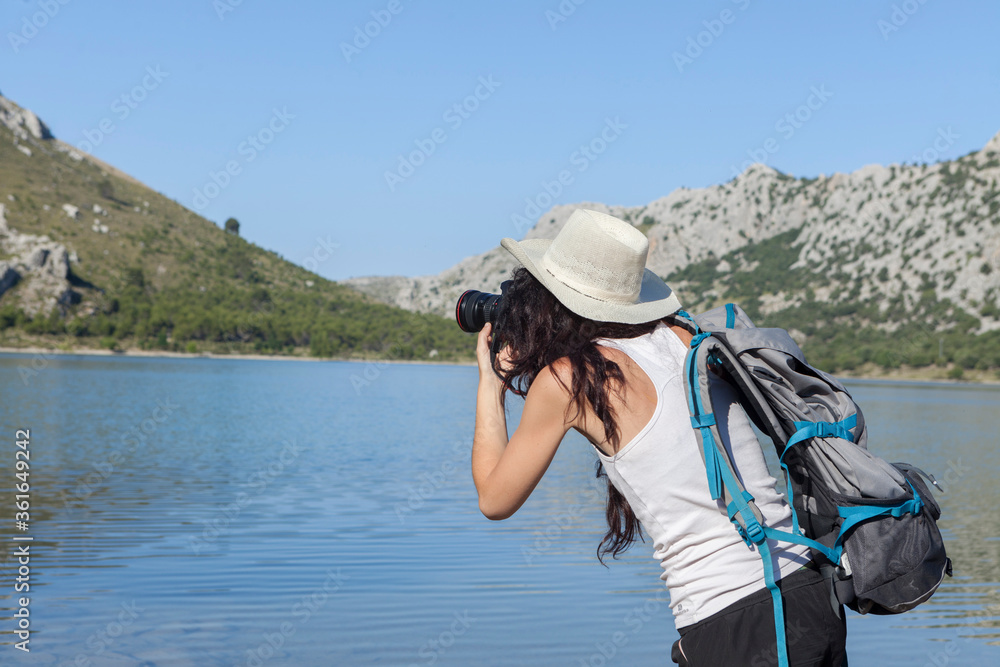 Wanderlust of a young woman, photographer and traveler. The woman is walking on the mountains and roads of the island of Majorca, the girl is wearing a hat and is taking photos. The woman is happy