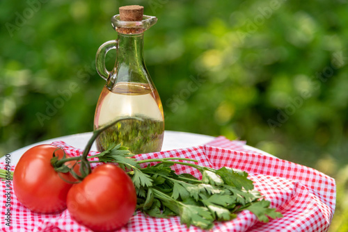 Sunflower oil in a glass bottle with ingredients for a summer salad on a background of green grass. Oil, herbs and tomatoes with space to copy.