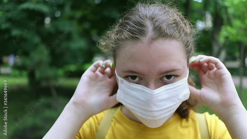 A teenage girl puts on a medical mask on a walk in a city Park A teenage girl puts on a medical mask on a walk in a city Park