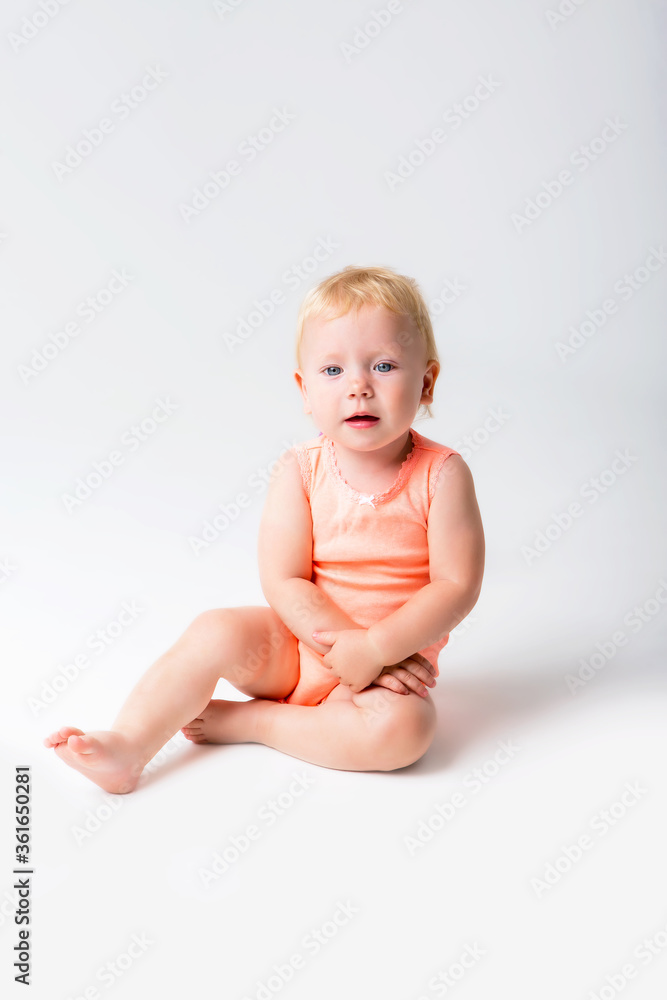 Toddler girl blonde laughs in orange bodysuit sitting on white background Toddler girl blonde laughs in orange bodysuit sitting on white background
