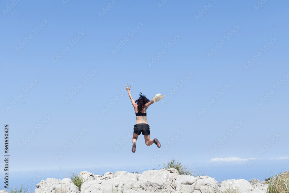 A girl traveling during the new normal of the summer holidays trekking through the mountains with views of the sky and the peaks, The girl is jumping with joy. Majorca island. A girl traveling during the new normal of the summer holidays trekking through the mountains with views of the sky and the peaks, The girl is jumping with joy. Majorca island.