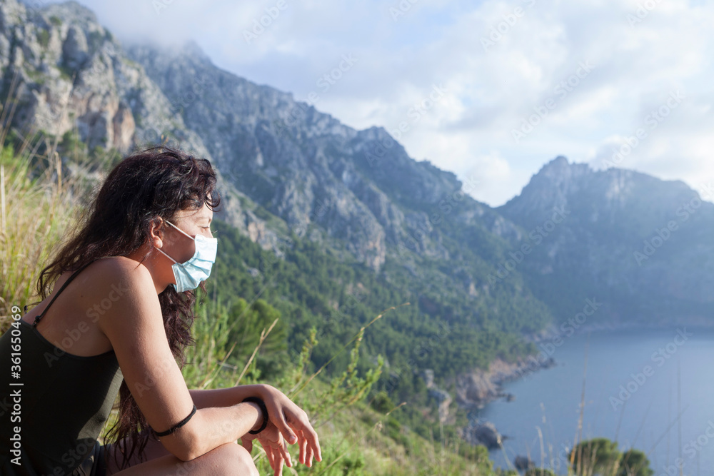 Wanderlust concept reopening of confinement. Portrait of a woman outdoors with surgical mask on her face at sunset, social distance in the mountains and the field. Back to normal, summer vacation 