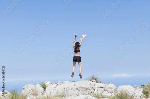 A girl traveling during the new normal of the summer holidays trekking through the mountains with views of the sky and the peaks, The girl is jumping with joy. Majorca island. © adradaguajardo