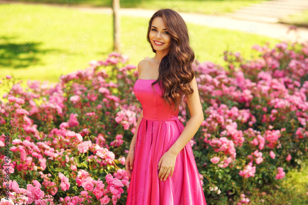 Princess. Young beautiful pretty woman posing in long evening luxury dress against bushes with pink roses on a sunny summer day. Vogue style fashion sensual portrait Princess. Young beautiful pretty woman posing in long evening luxury dress against bushes with pink roses on a sunny summer day. Vogue style fashion sensual portrait