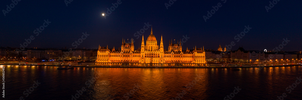 Panoramic aerial drone shot of front facade of Hungarian Parliament with lights on in Budapest night