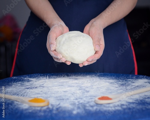 Panadero sostienen la masa en sus manos. Preparación de masa sobre la mesa azul con harina salpicada y condimentos en cucharas de madera. photo