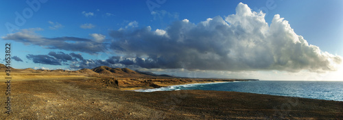View on a coastline with huge rocks and sandy beach on a sunny evening with soft light. Mountains at horizon and clouds at the sky