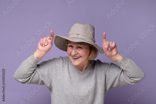 Cheerful middle aged woman i nsummer hat finding new idea and raising index finger. Mature woman pointing up at copy space. Advertising or new idea photo