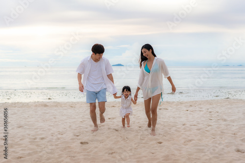 Happy Asian family holidays during joyful father, mother and daughter walking together along summer sunset sea. Happy family travel on beach in holiday, Summer and vacation.