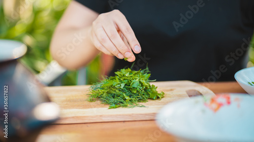 Close up of women's hands plucks greens from sticks and puts them on cutting board.