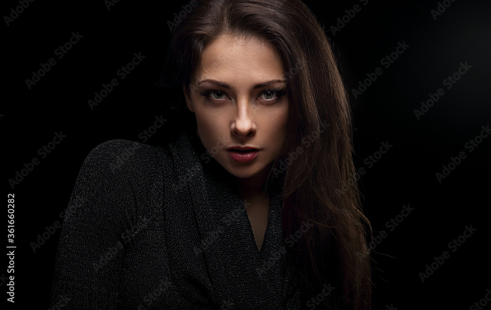 Sexy makeup woman with natural angry emotion posing isolated on dark shadow black background. Closeup portrait in deep low key light shadows. Sexy makeup woman with natural angry emotion posing isolated on dark shadow black background. Closeup portrait in deep low key light shadows.