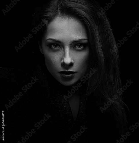 Sexy vamp woman with natural angry emotion posing isolated on dark shadow black background. Closeup portrait in deep low key light shadows. Art.