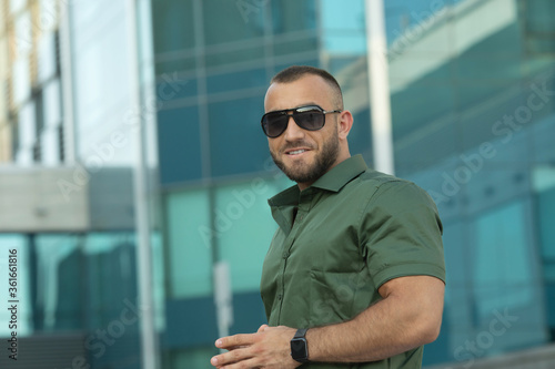 Confident handsome man in sunglasses and shirt over city background. Men's beauty, fashion. Outdoor portrait.