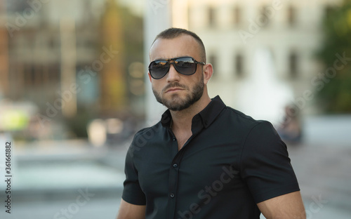 Confident handsome man in sunglasses and shirt over city background. Men's beauty, fashion. Outdoor portrait.