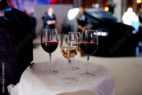 waiter with a tray with glasses of red and white wine on a white napkin. The car under the cover is in the background.