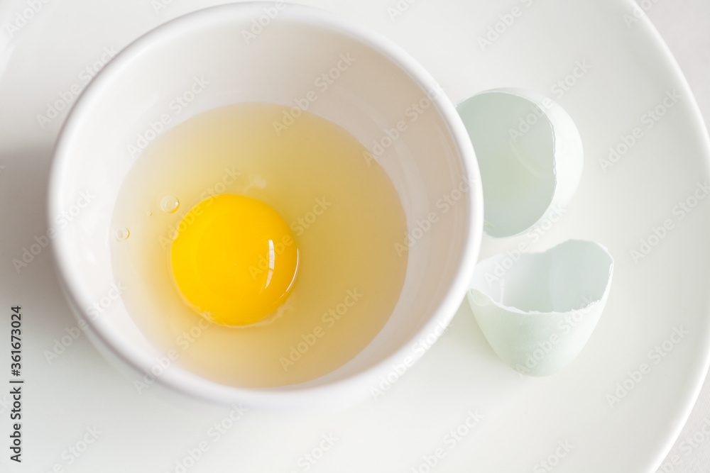 Raw whole egg in bowl and cracked eggshell on plate food ingredient Raw whole egg in bowl and cracked eggshell on plate food ingredient