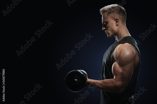 Athletic man in training pumping up muscles with dumbbell. Strong bodybuilder with perfect deltoid muscles, shoulders, biceps, triceps and chest. Close-up of a power fitness man. photo