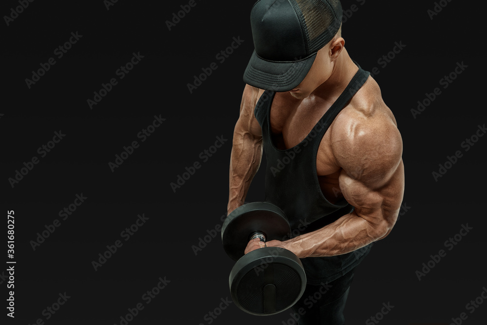 Close up shot of muscular bodybuilder wearing a red tank top and black cap doing biceps curl with dumbbell against black background. Image with clipping path