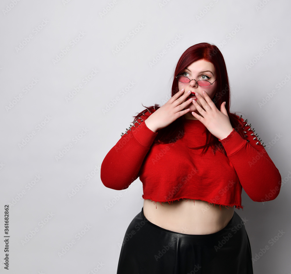 Plus size ginger girl in red top, black skirt, sunglasses. Covered mouth with hands, looking scared, posing isolated on white Plus size ginger girl in red top, black skirt, sunglasses. Covered mouth with hands, looking scared, posing isolated on white