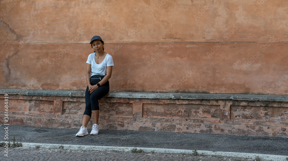 Woman in cap sitting on bench in front of beautiful teracota wall Woman in cap sitting on bench in front of beautiful teracota wall