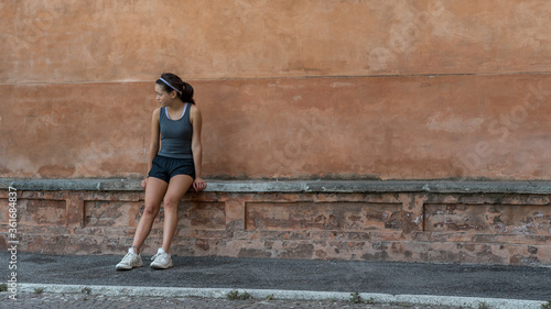 Young teen girl with headband, shorts, tanktop and sneakers sitting on brick bench