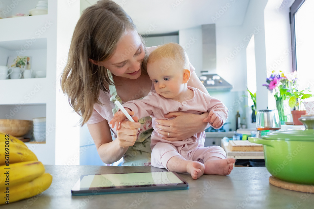 Mom and baby daughter cooking together at home, watching recipes on tablet. Child care or cooking at home concept Mom and baby daughter cooking together at home, watching recipes on tablet. Child care or cooking at home concept